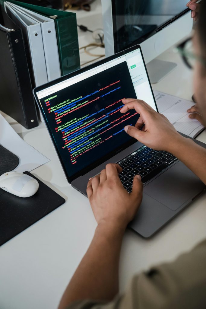pexels photo 12899188 12899188 Close-up of a programmer pointing at a colorful code script on a laptop in an office setting.